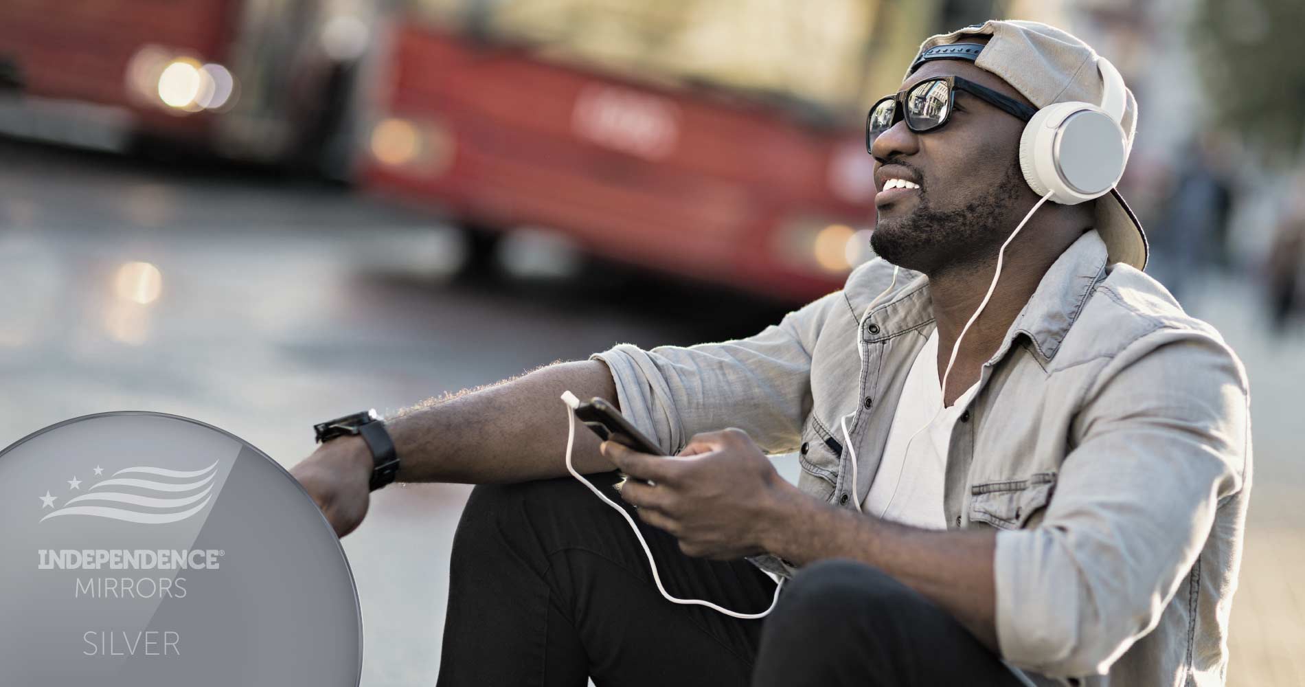 Man sitting on the curb listening to music with headphones, wearing silver-colored mirrored sunglasses